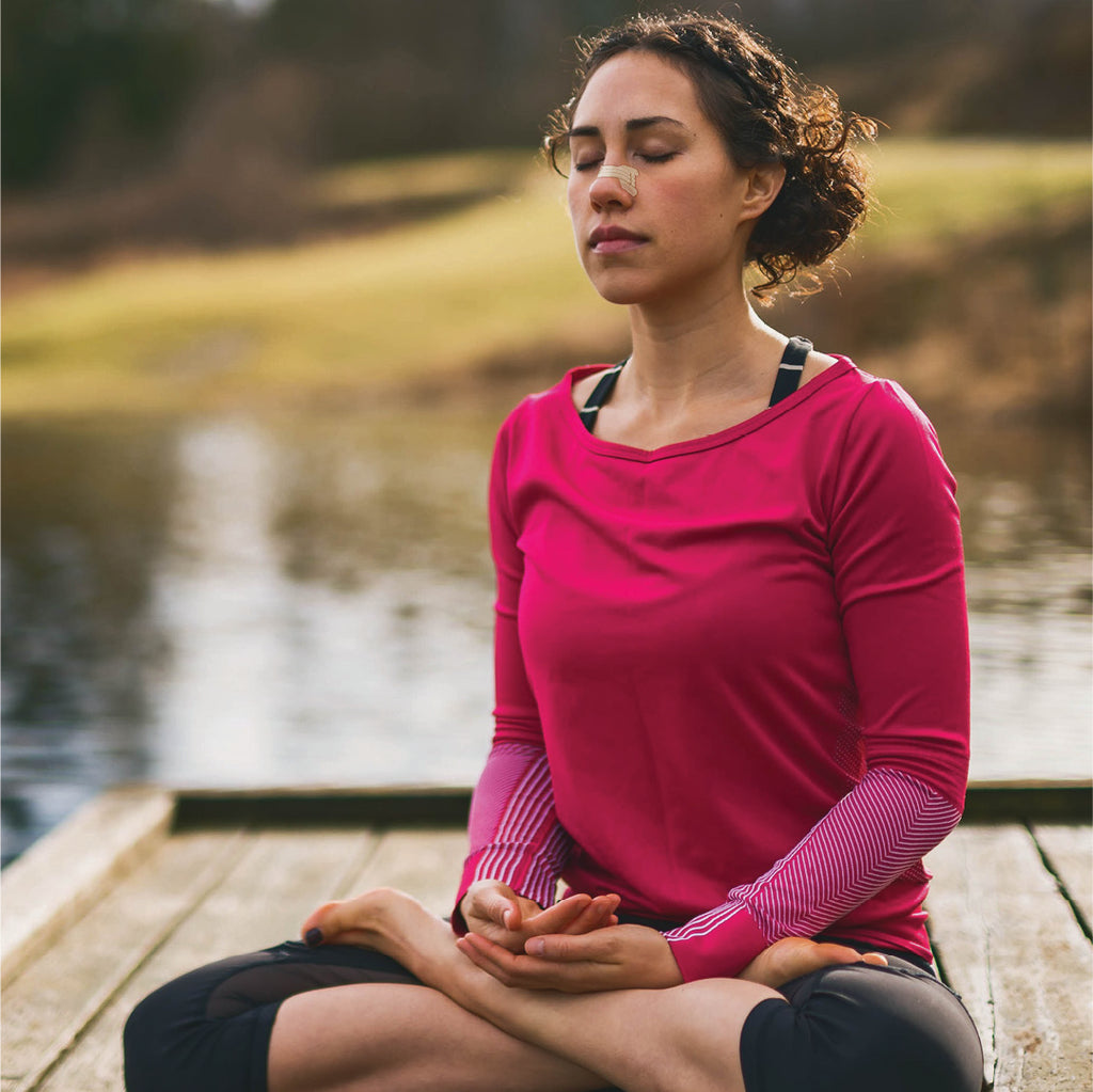 woman using a clear passage nasal strip to practice yoga by a lake