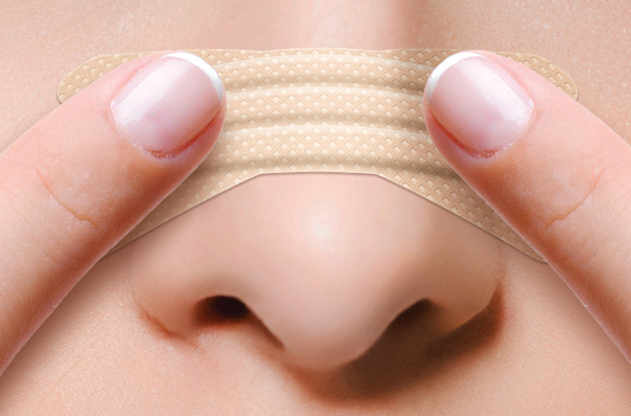 a persons nose with a clear passage nasal strip already applied and a persons fingers showing to hold and rub the strip for proper adhesion