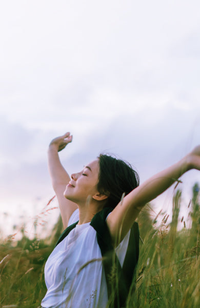 Woman laying in a field with her arms up while wearing a clear passage nasal strip and feeling relieved